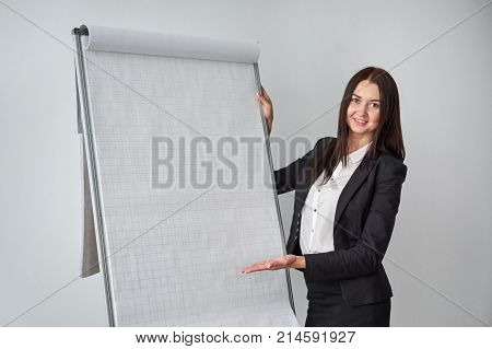 Portrait of young smiling businesswoman standing by flipchart in office.