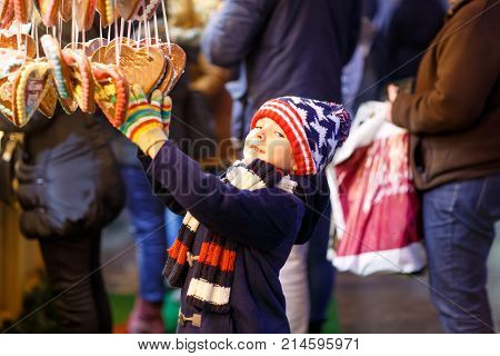 Little cute kid boy buying sweets from a cancy stand on Christmas market. Happy child on traditional family market in Germany. Preschooler in colorful winter clothes.