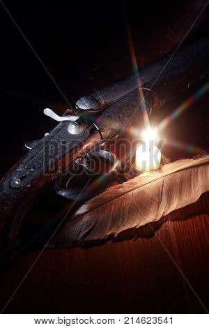 Ancient hunting shotgun closeup on wooden board near lighting candle