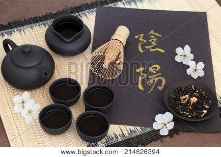 Chinese jasmine tea with yin and yang chinese calligraphy script, cherry blossom, teapot, cups, jug, whisk and dried leaves on bamboo mat. Translation reads as yin yang.