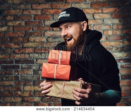 The positive Redbeard male holds Christmas gifts over the wall of a brick.