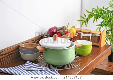 Stewpan, bowls and vegetables on wooden table in kitchen