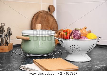 Colander with vegetables and stewpan on table in kitchen