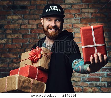 The positive Redbeard male holds Christmas gifts over the wall of a brick.