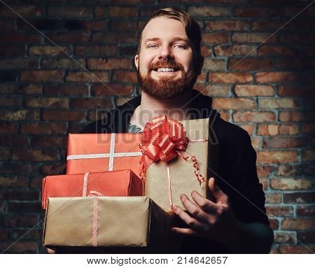 The positive Redbeard male holds Christmas gifts over the wall of a brick.