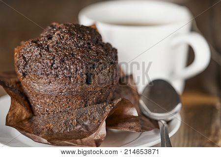 Delocious chocolate muffin with a cup of tea and a spoon on the wooden table close up