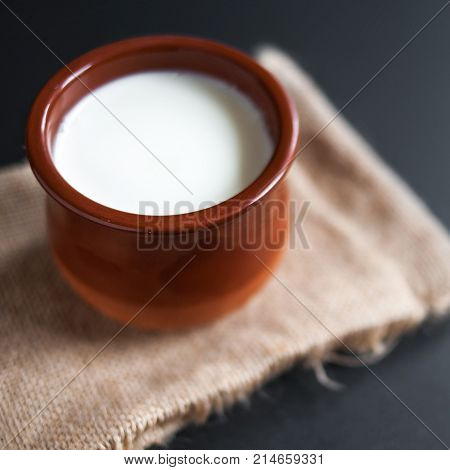 Sour cream or natural Cottage cheese curd in clay pot on dark background. Traditional Cuajada yogurt cream