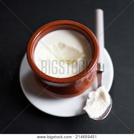 Sour cream or natural Cottage cheese curd in clay pot on dark background. Traditional Cuajada yogurt cream