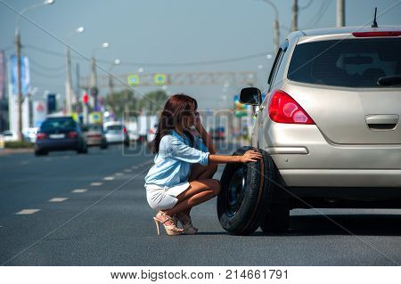 Pretty red-haired girl in shorts and high heels sat down to her broken car and talked on the phone waiting for help on the highway.
