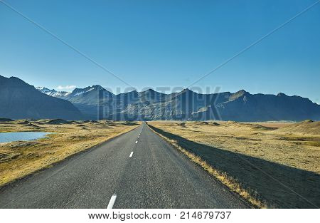 Travel to Iceland. road in a bright sunny mountain landscape. Vatna volcano covered with snow and ice on tne background.