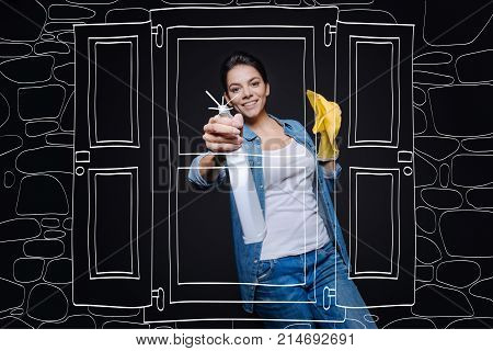 Make with inspiration. Cheerful delighted smiling housewife holding rag and cleaning window while doing spring cleaning