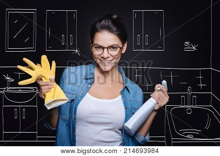 No dirt. Positive beautiful woman holding spray and doing spring cleaning while expressing gladness