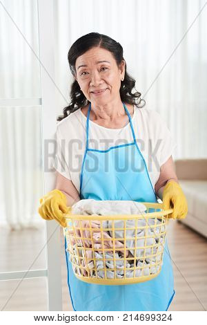 Smiling aged Vietnamese woman with laudry basket full of dirty clothes