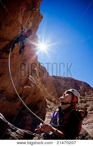 Bir kadın dağcı lider bir kaya tırmanışı Todra Vadisi, Atlas, Maroc, Afrika boyunca belays.