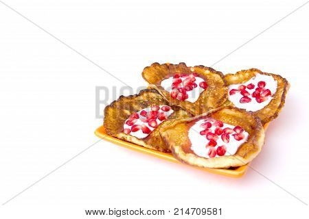 Fritters on a white background on a plate. Pancakes on an orange plate with sour cream, jam and pomegranate.