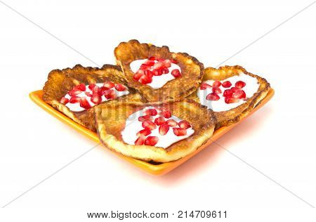 Fritters on a white background on a plate. Pancakes on an orange plate with sour cream, jam and pomegranate.