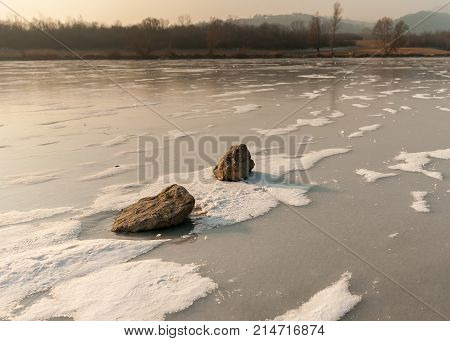 Stones Lying On Frozen River With Spots Of Light Snow