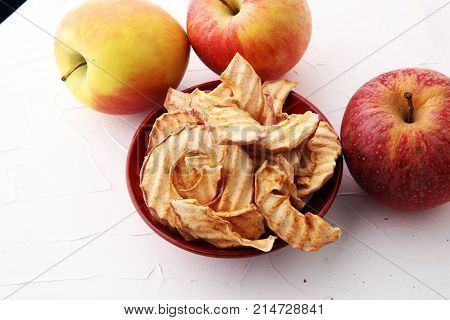 Dehydrated apples chips in bowl and apples on white background.