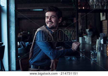 Successful and stylish. Handsome young man looking away with smile while sitting in loft
interior at bar counter