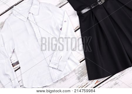 Girls school clothes, wooden background. White cotton shirt and black dress for school wear. Traditional school clothes for girls.