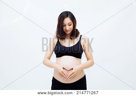 Pregnant woman making a heart shape hand gesture on her pregnant belly over white isolated background