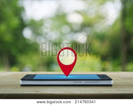 Map pin location button on modern smart phone screen on wooden table over blur green tree in park Map pointer navigation concept