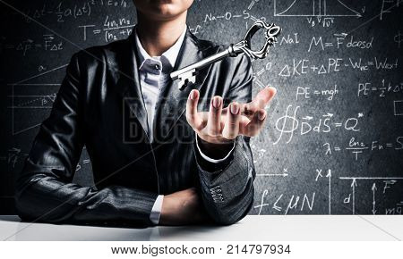 Cropped image of businessman in suit keeping big key in hand with business sketches on dark wall on background.