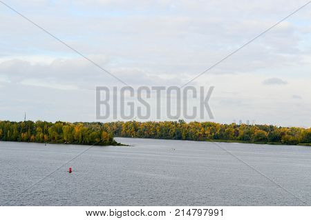 A lonely red buoy floats against the background of trees on the shore. Landscape.