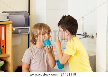 Two kids in classroom boys drinking water in school holding plastic glasses