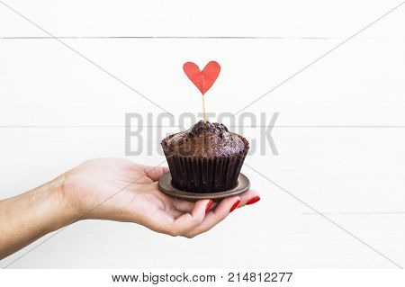 Valentine's Day concept. A woman holds a chocolate capcake in her hand with a paper heart on a stick.