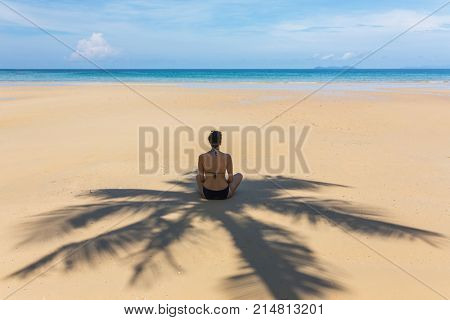 Young woman sitting in the shadow of palm tree on tropical beach on Koh Kood island, Thailand