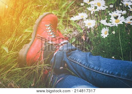 Person wearing hiking boots lying in a meadow with white spring daisies and golden glow from the sun in a close up view of the feet