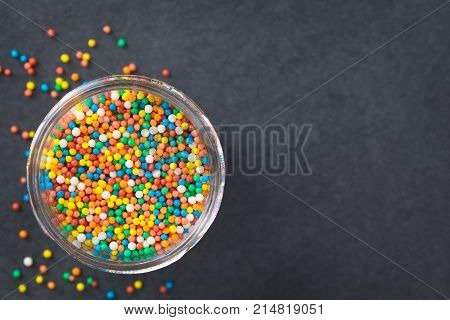 Colorful nonpareils sugar sprinkles in glass jar photographed overhead on slate (Selective Focus Focus on the nonpareils in the jar)