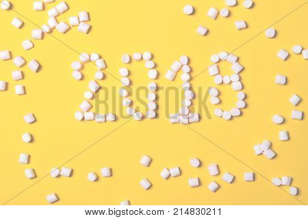 Christmas composition concept of new year. Marchmalow in form of an inscription 2018 on yellow old stily background