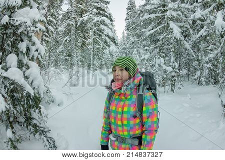 Happy Tourist Girl With A Backpack Walks In A Winter Forest Among Large Trees