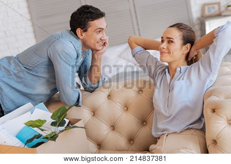 Pleasant morning. Nice loving couple looking happy while being at home and smiling to each other while a big box with personal items standing next to them