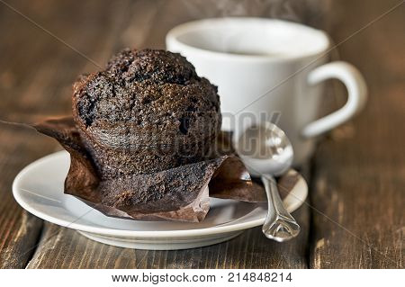 Delocious chocolate muffin with a steaming cup of tea or coffee on the wooden table close up