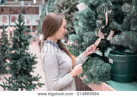 Cheerful happy customer girl choosing Christmas tree for the new year on Christmas Eve. difficult decision. Various choice