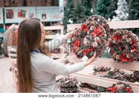 customer girl choosing Christmas decorations. difficult decision. Various choice of New Year's wreath with decorations
