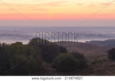 Morning autumn landscape: fog over hills and forest on background of red sunrise. View from above. Village Opishnya Poltava region Ukraine