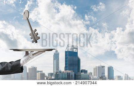Closeup of waiter's hand in white glove presenting stone key symbol on metal tray with cityscape view on background. 3D rendering.