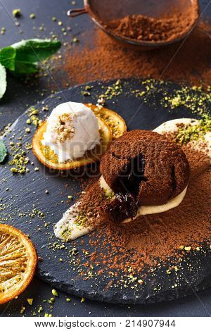 Exquisite french dessert. Chocolate fondant, creme anglaise and vanilla ice cream, sprinkled with cocoa powder, served on round slate finely decorated with orange citron and pistachio crumble, closeup