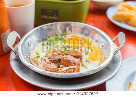 A pan fried egg with toppings on the red table is breakfast of asian food.