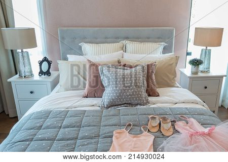Ballet set and many pillow on a girl bed with bedside lamp in warm light bedroom.