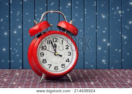 Red retro alarm clock at twelve o'clock against the background of blue walls and flying snow. Midnight midday. Minutes about New year.