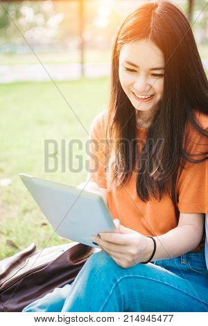 A young or teen asian girl student in university smiling and reading the book and look at the tablet or labtop computer in summer holiday.