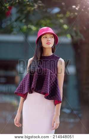 Attractive asian woman fashion portrait. Beautiful romantic mixed race asian caucasian young girl in pink hat skirt, jaket looking away outdoor against blurred bokeh city background. Gorgeous slim model in trendy glamour stylish clothes waiting someone ou