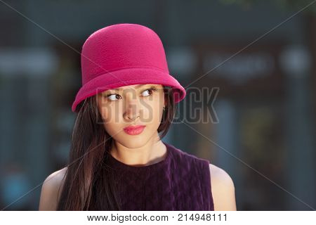 Attractive asian woman fashion portrait. Beautiful romantic mixed race asian caucasian young girl in pink hat jaket looking away outdoor against blurred bokeh city background. Gorgeous slim model in trendy glamour stylish clothes waiting someone outside i