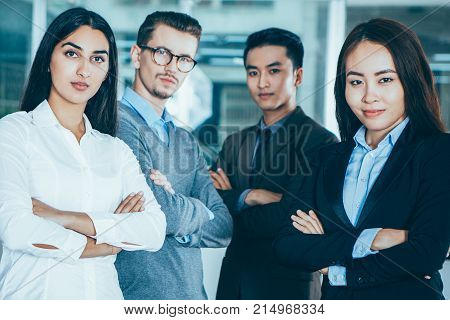 Closeup portrait of four proud young business people looking at camera and standing with arms crossed and cafe interior in background