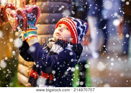 Little cute kid boy buying sweets from a cancy stand on Christmas market. Happy child on traditional family market in Germany. Preschooler in colorful winter clothes.